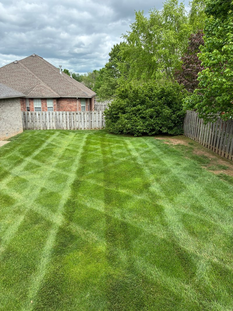 Diamond-pattern backyard cut on a residential lawn beside a brick house and wooden fence.